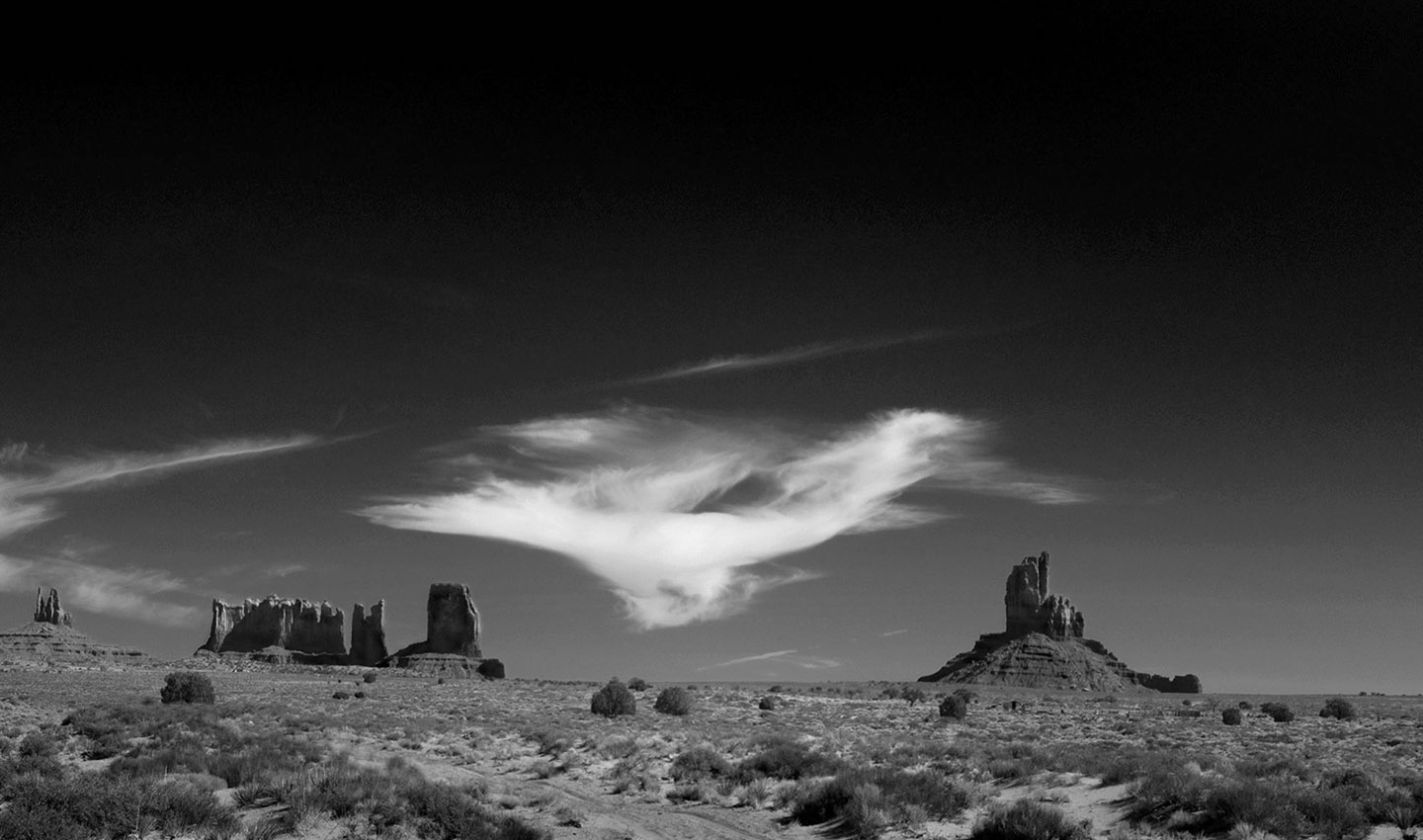 Navajo Sky is a dramatic view of Monument Valley under a darkened sky with a single white cloud evoking a spiritual horse.